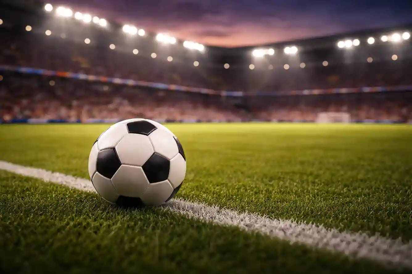 Ballon de football posé sur une pelouse verte de stade avec les projecteurs allumés en arrière-plan